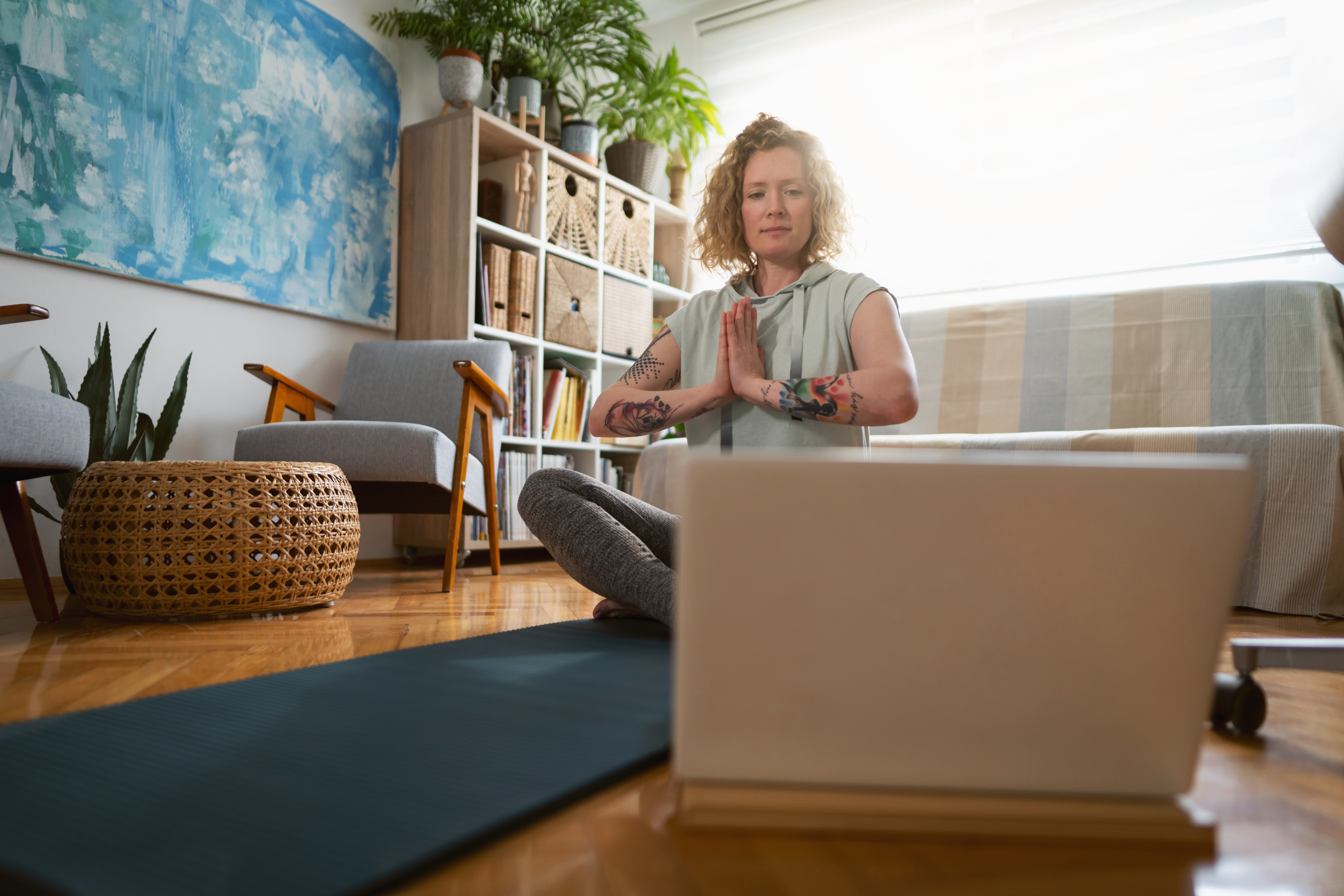 While watching online yoga class on laptop, Caucasian young woman in lotus position meditating