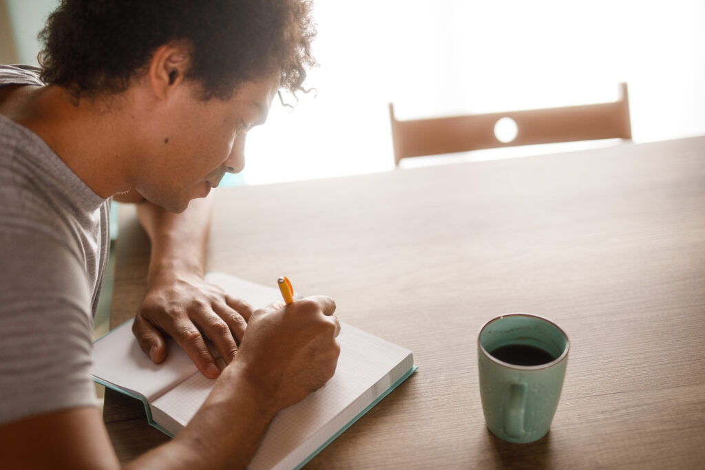 Headshot of organized mid adult man sitting at dining table, enjoying a cup of coffee and writing a ''to do list''.